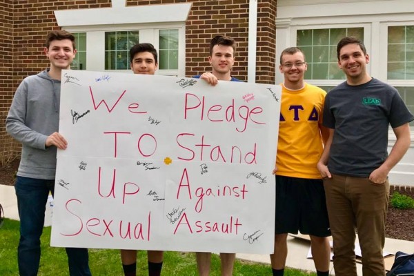 Five people holding a poster that reads "We Pledge To Stand Up Against Sexual Assault"